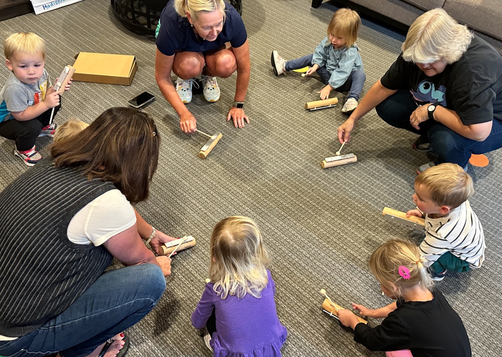 Toddlers sitting in a circle playing rhythm instruments with their teachers