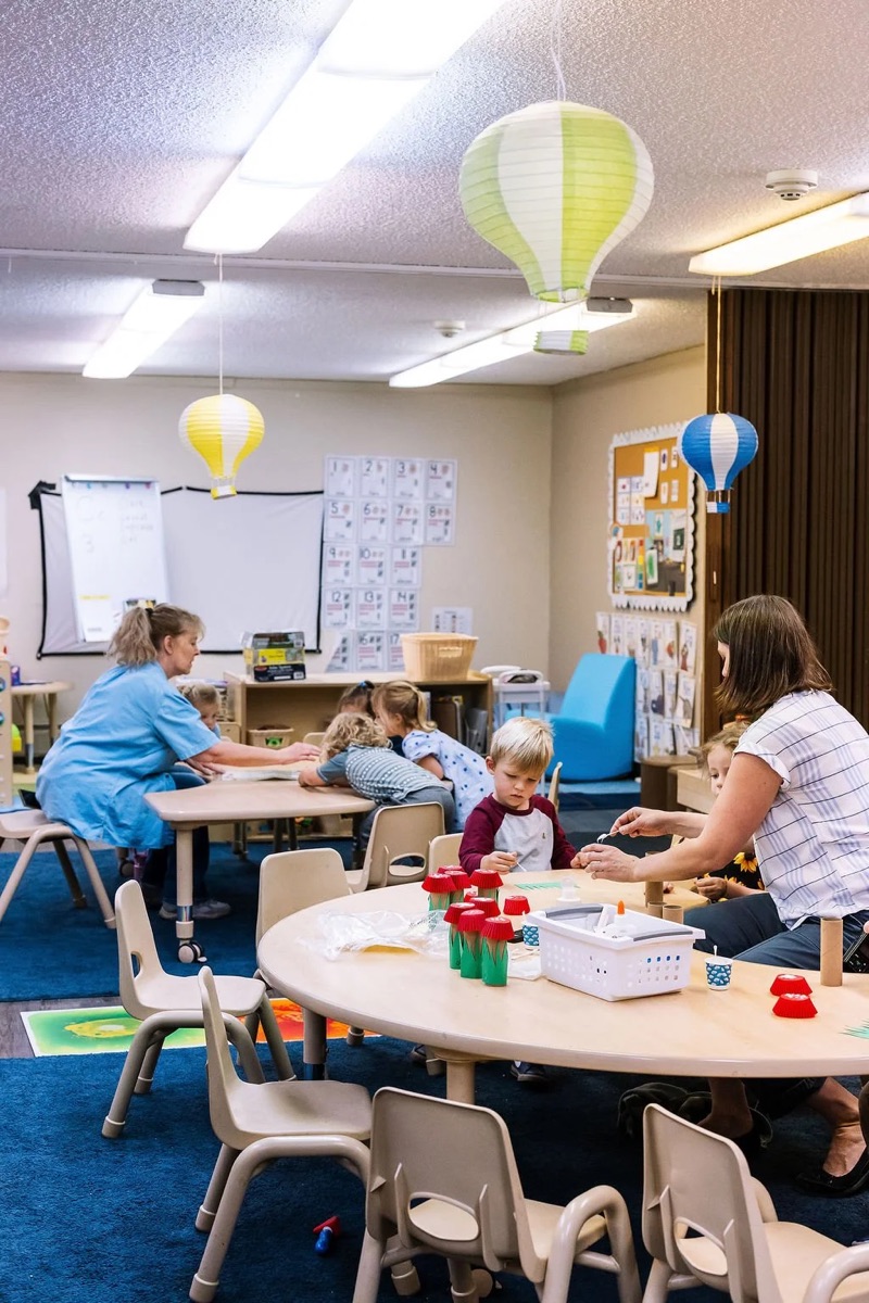 Preschoolers working at round tables with teachers under paper lanterns