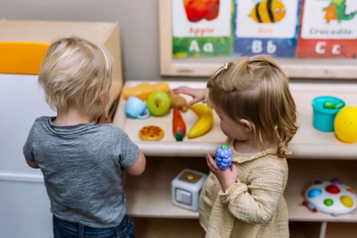 Two toddlers playing with pretend fruit at a play kitchen