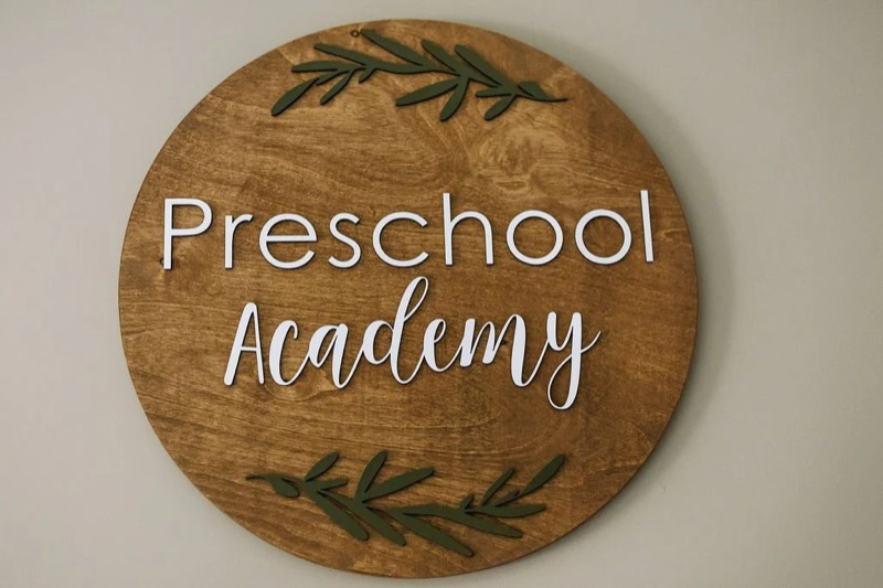 A round wooden Preschool Academy sign decorated with green leaves